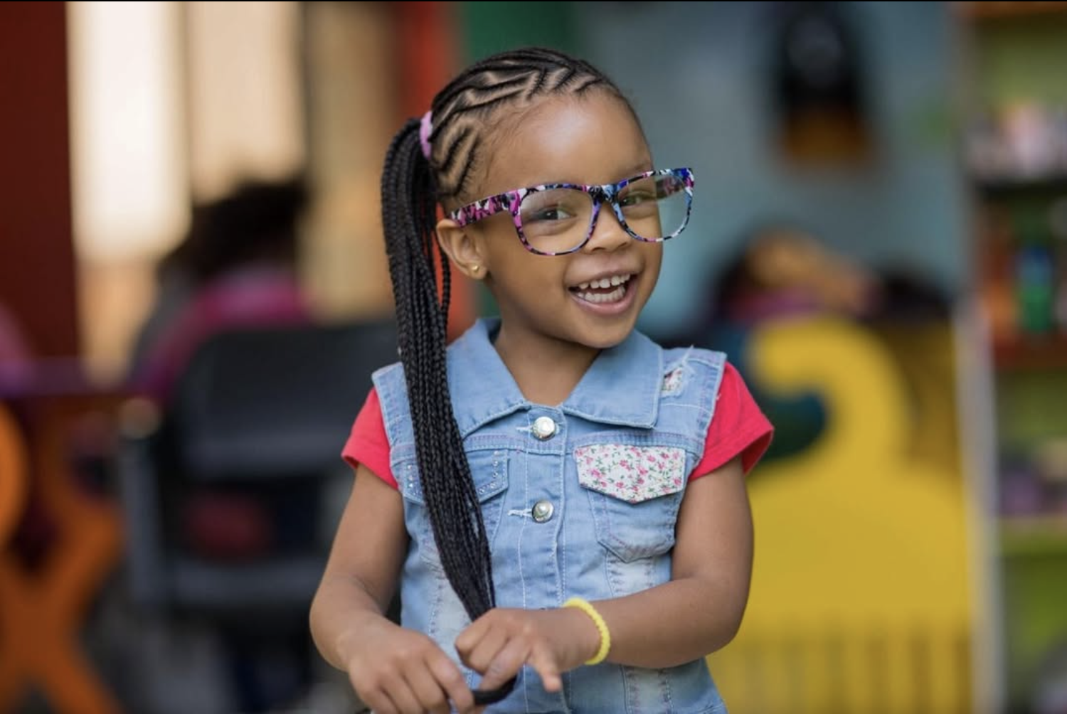 Smiling young girl with braided hair and colorful glasses at Kids' Nook